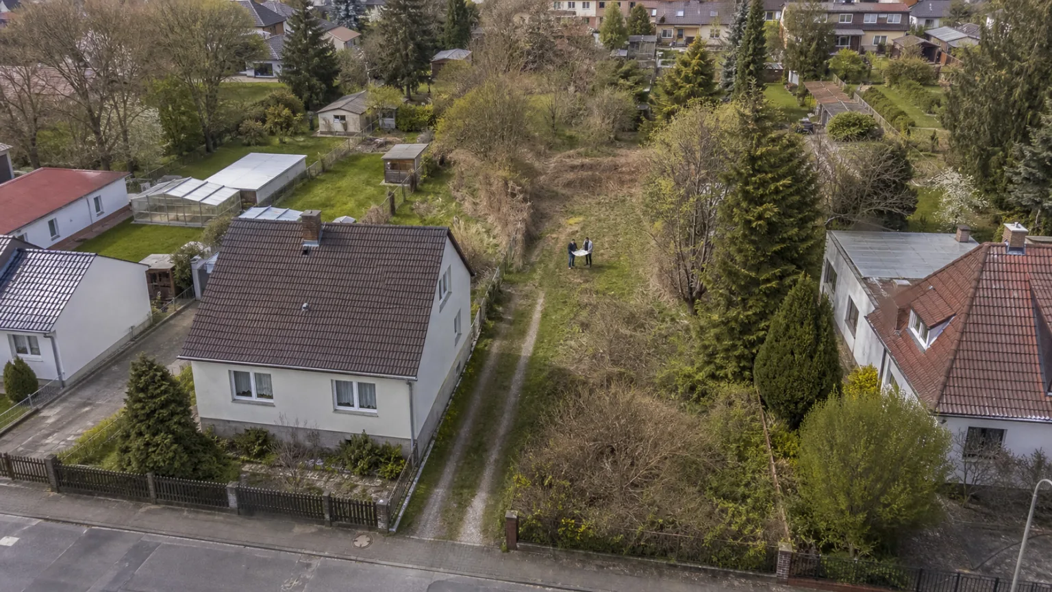 Blick auf ein tiefes Wohngrundstück mit seitlicher Zufahrt und unbebauter Fläche in zweiter Reihe